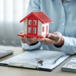 Female real estate agent is use hands holding house of red roof for the concept of real estate